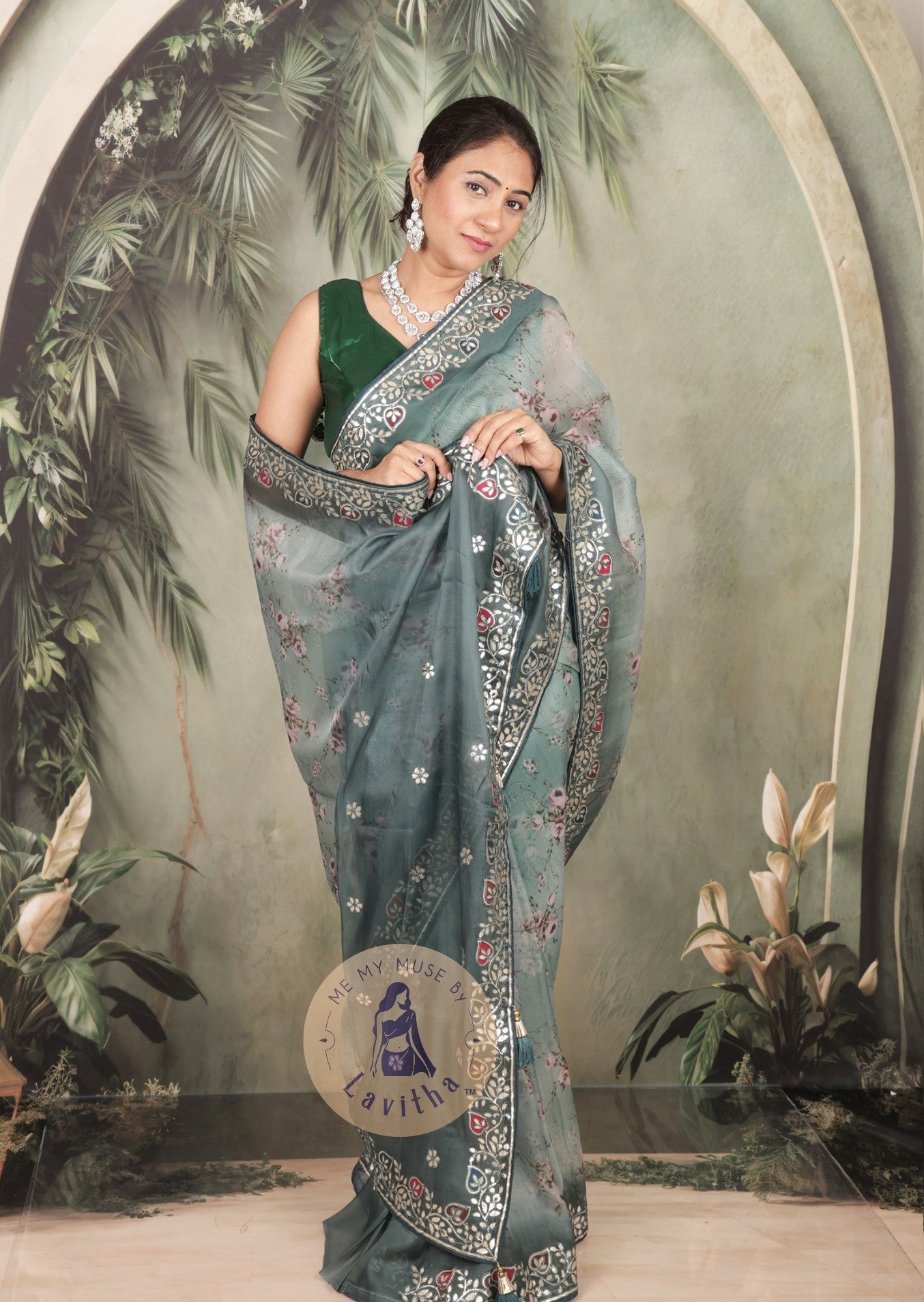 Our muse is wearing a rich premium floral digital printed organza Pastel Greyish Green saree with Gota Patti work on the border and designer pallu. This festive-wear saree is part of the Dilqash collection of Me My Muse by Lavitha